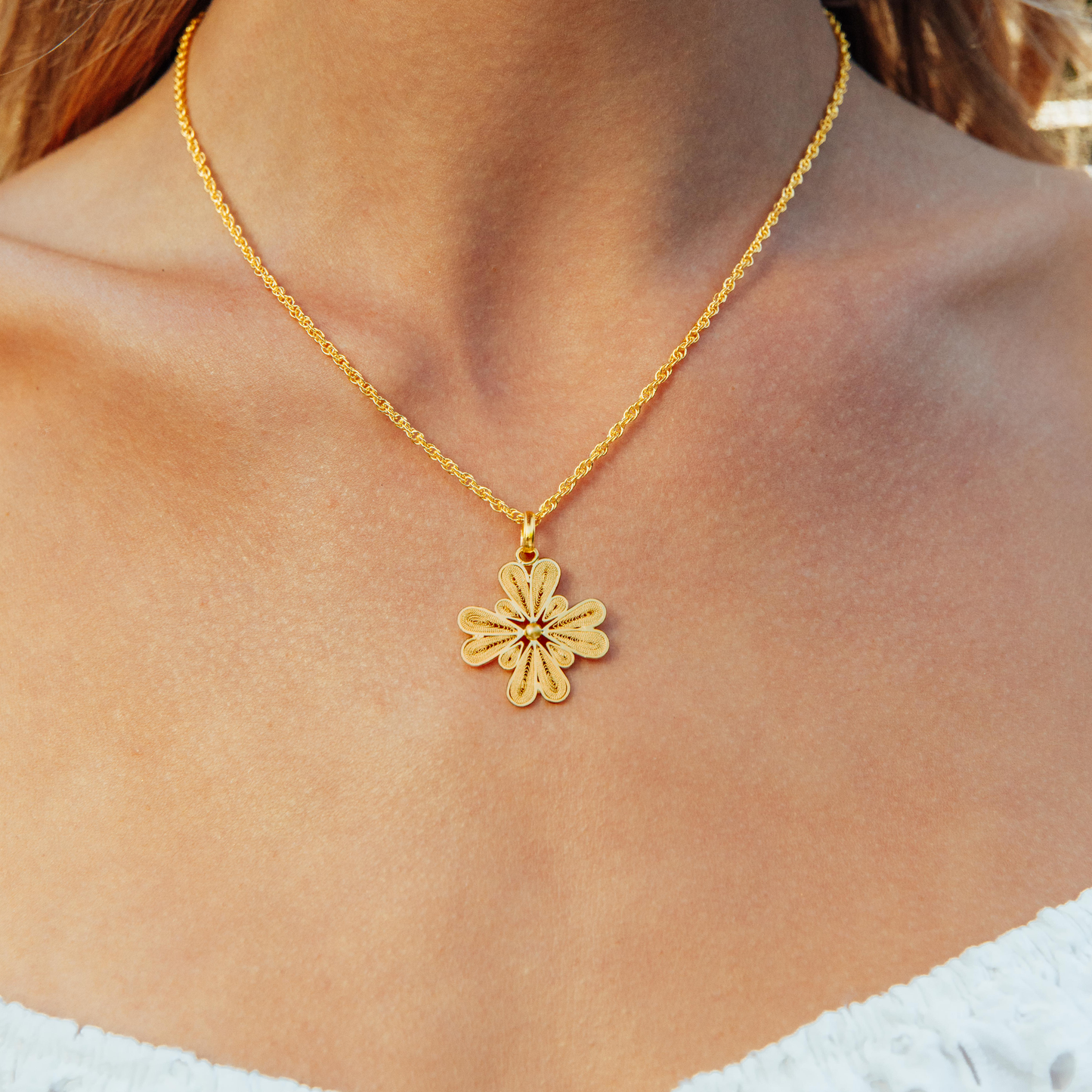 Close-up of a handmade 18K gold vermeil filigree flower necklace by Oh Voila Jewelry, styled with a white off-the-shoulder top.